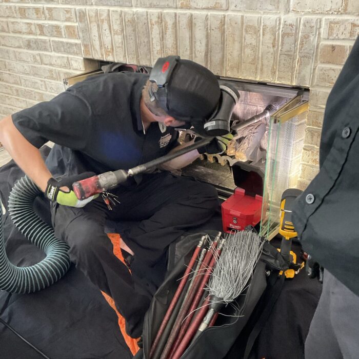 A professional Orlando chimney sweep technician uses specialized rotary power tools to clean the interior fireplace flue, with specialized brushes and a vacuum hose nearby on a drop cloth.
