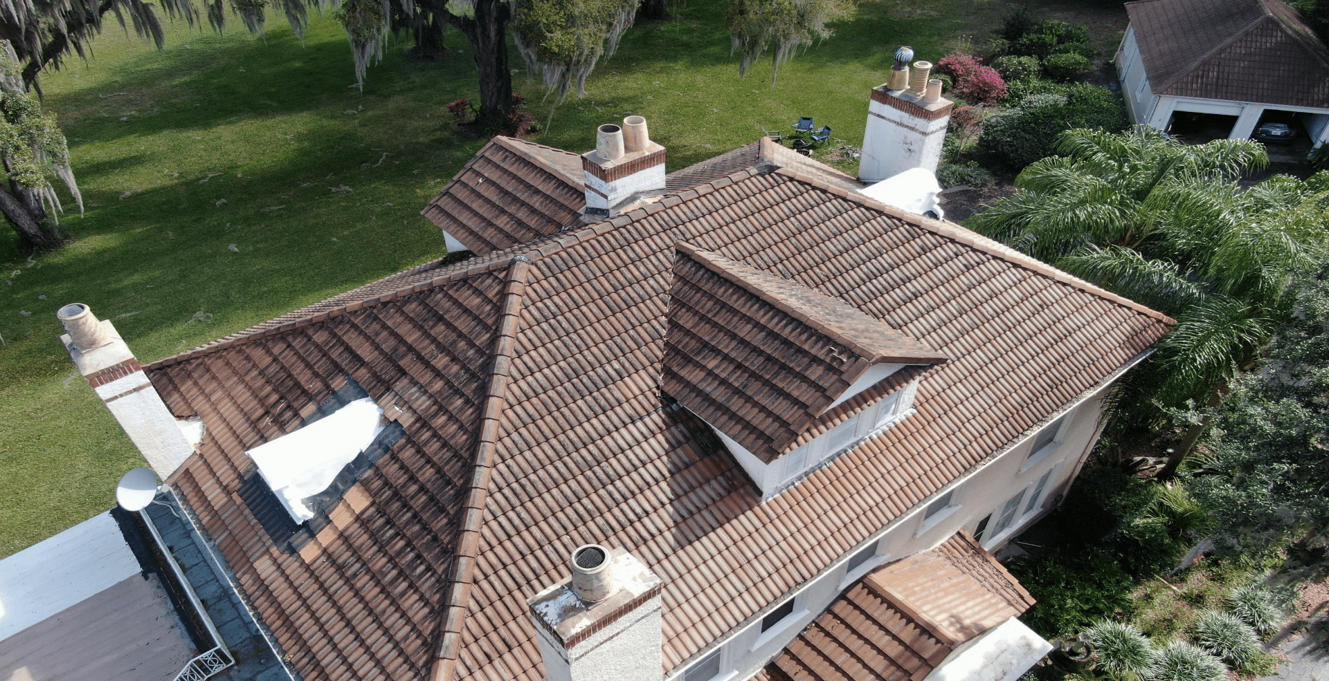 An aerial view of a large residential home featuring a brown tile roof and multiple chimneys, showcasing a target area for a professional dryer vent inspection in Orlando, FL.
