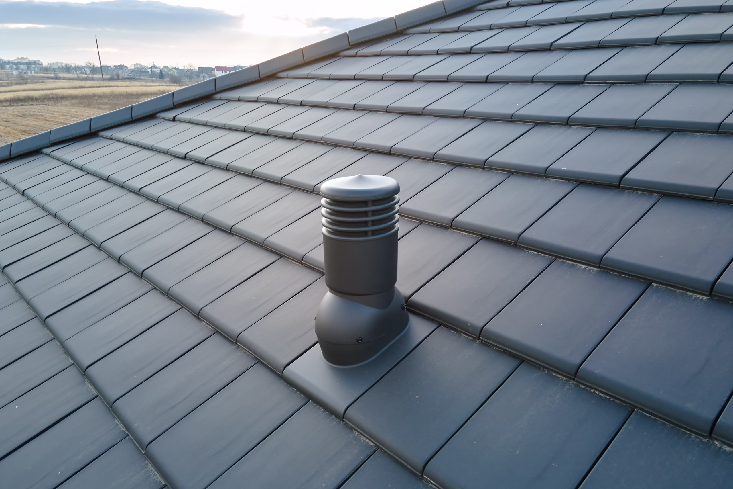 Closeup of ventilation pipe on house roof top covered with ceramic shingles. Tiled covering of building