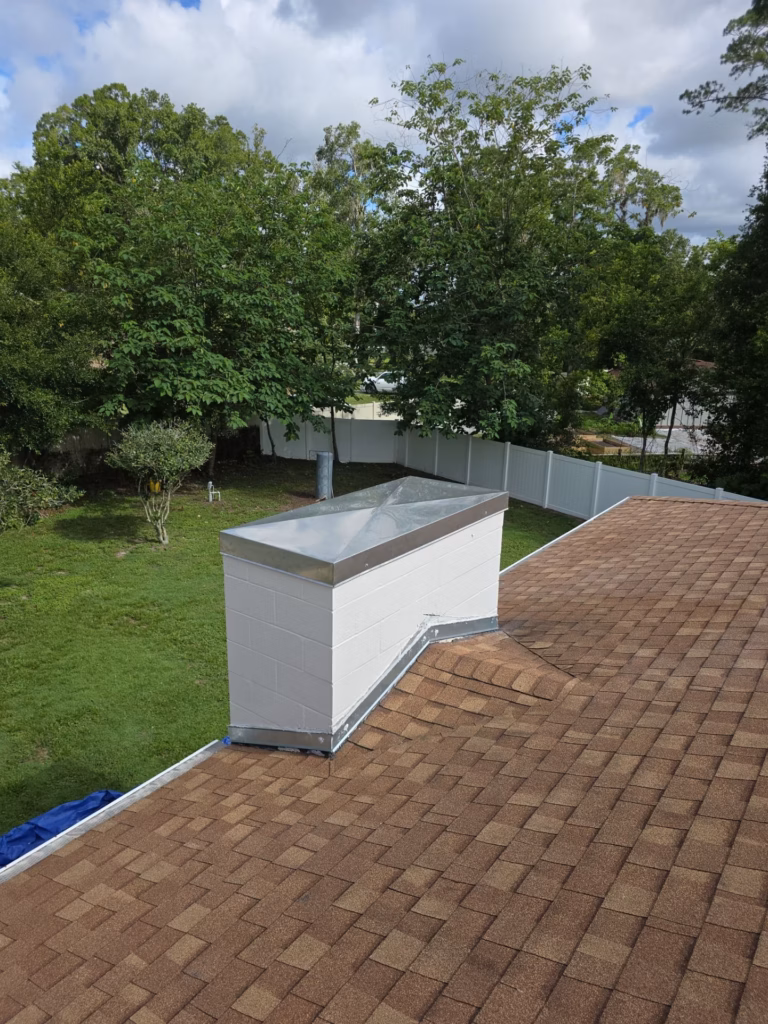 A newly installed stainless steel chimney chase cover on a white siding chimney box over a shingle roof in High Springs, FL.