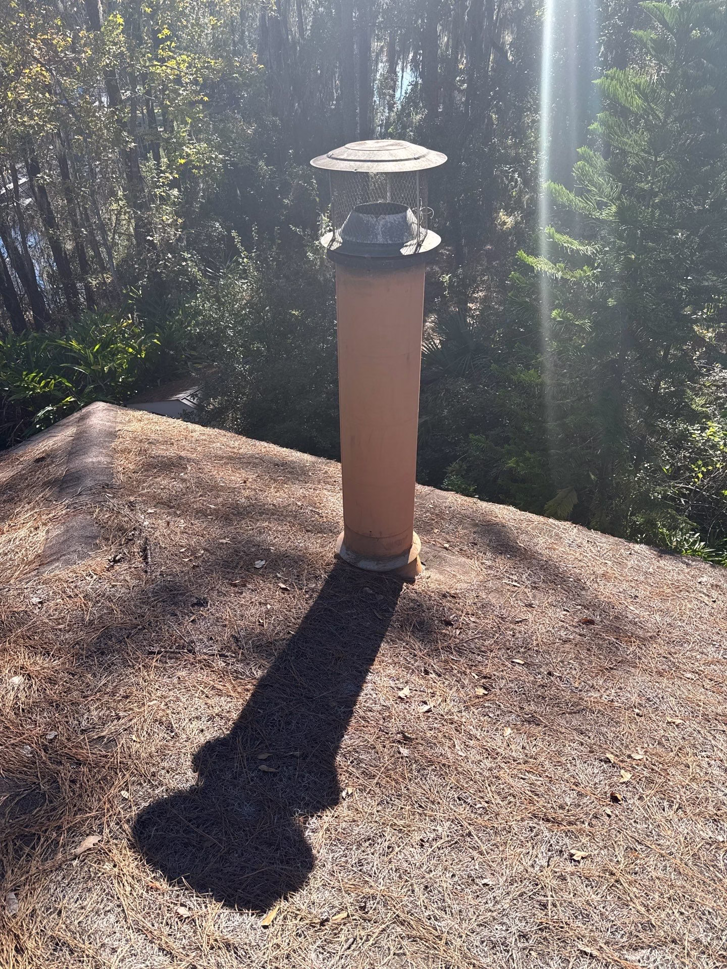 Chimney Caps 1 Tall terra cotta clay flue pipe with a metal spark arrestor cap installed on a roof in High Springs, FL.