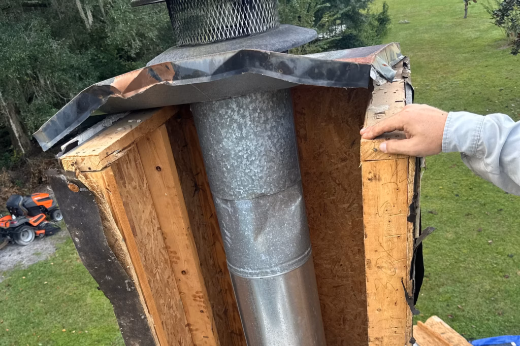 Exposed wood chimney chase structure showing an internal metal flue pipe during a chase cover replacement in Gainesville, FL.