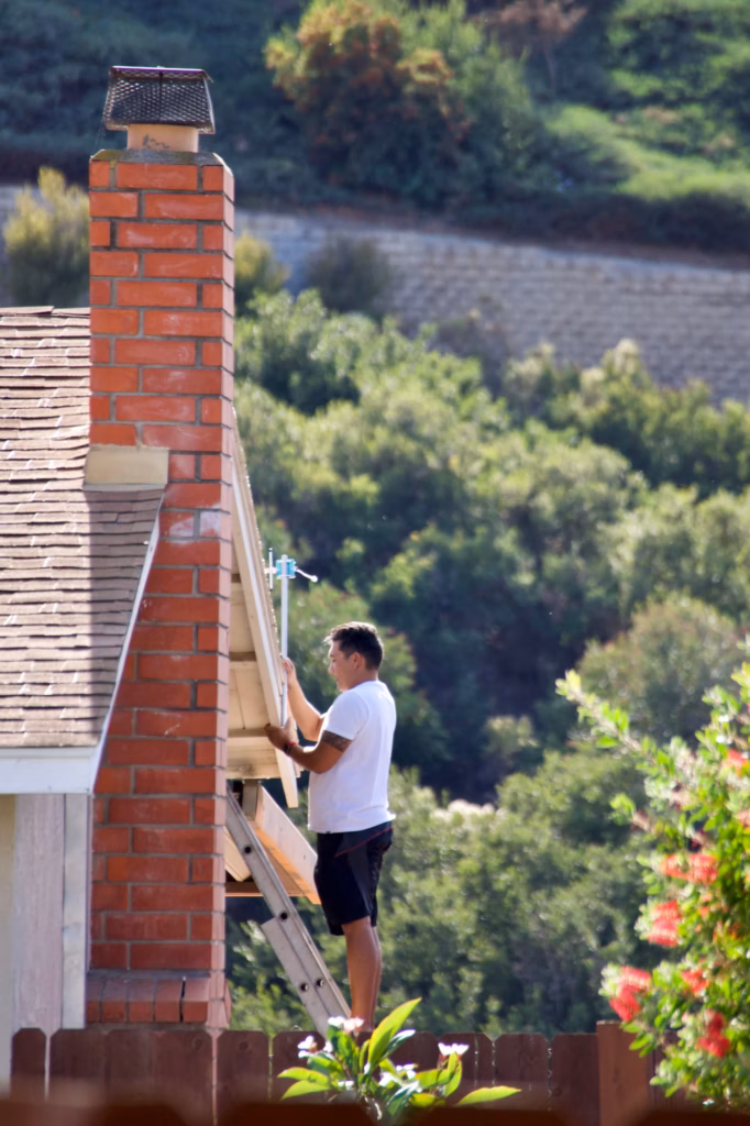 Technician working on an exterior ladder next to a tall red brick chimney with a metal cap in Ocala, FL.
