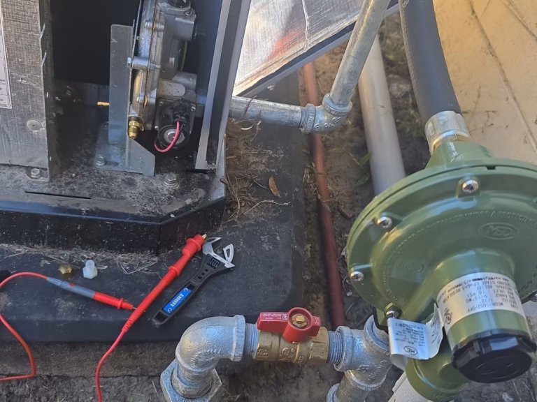 A green gas pressure regulator and red shutoff valve connected to galvanized piping next to an open equipment panel and multimeter testing gear in High Springs, FL.