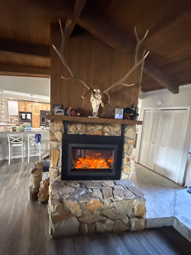 A rustic stone fireplace with an electric fireplace insert, stone hearth bench, wooden mantle, and animal skull mounted above in Gainesville, FL.