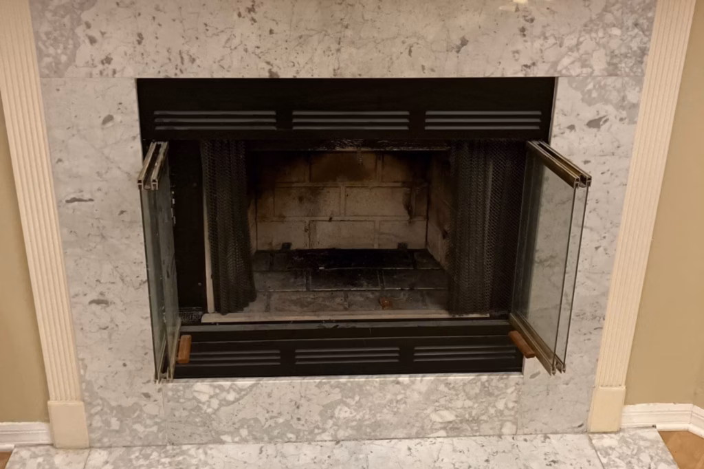 Open glass doors of an indoor woodburning fireplace with a marble hearth and surround in a Ocala, FL home.