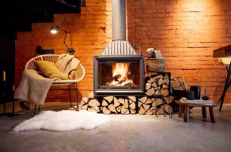 A modern woodburning fireplace installation in Gainesville, FL, with glowing flames inside a glass enclosure, neatly stacked firewood underneath, set against an exposed red brick wall.