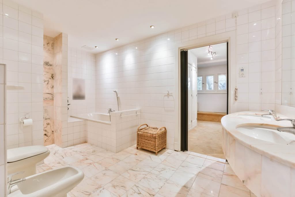 Remodeled bathroom with white tile walls, marble floors, a built-in tub and a double marble vanity by Always Home Repair