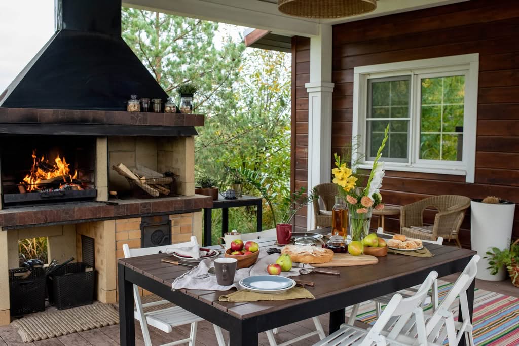 Covered outdoor patio with a brick fireplace and dining area by Always Home Repair